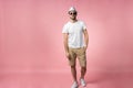 Full length of attractive confident young man in hat standing with hands in pockets over pink background. Royalty Free Stock Photo