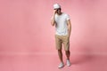 Full length of attractive confident young man in hat standing with hands in pockets over pink background. Royalty Free Stock Photo