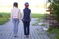 Full length back view of two children, girl with long braids and boy in casual clothing standing very straight on grassy pavement