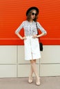 full-length beautiful young woman model wearing white striped shirt, black handbag clutch, round hat, skirt on city street over Royalty Free Stock Photo