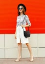 full-length beautiful young woman model wearing white striped shirt, black handbag clutch, round hat, skirt on city street over Royalty Free Stock Photo