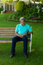 Full length of biracial senior man reading book while sitting on bench against plants in park Royalty Free Stock Photo
