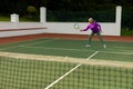 Full length of biracial senior woman hitting tennis ball with racket while playing tennis at court Royalty Free Stock Photo