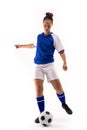 Full length of biracial young female soccer player kicking soccer ball against white background Royalty Free Stock Photo