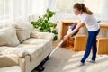 Full length body portrait of young woman in white shirt and jeans cleaning carpet with vacuum cleaner in living room, copy space. Royalty Free Stock Photo