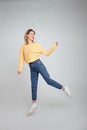 Full length body shot of joyful pleased young female model jumps happily in air against white background, wears, sweatshirt, jeans