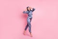 Full length body size photo of brunette in blue pajama jumping smiling touching sleeping mask isolated on pastel pink