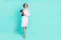 Full length body size photo of curious nurse smiling going forward keeping clipboard isolated vibrant teal color