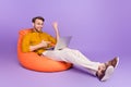 Full length body size photo of guy sitting in beanbag using laptop having video meeting on vivid violet color