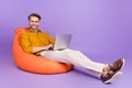 Full length body size photo of guy sitting in beanbag using laptop on vivid purple color background