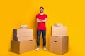 Full length body size photo happy courier with crossed hands packing delivery boxes isolated on vivid yellow color