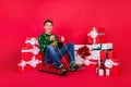 Full length body size photo happy guy in ugly sweater smiling sitting on sledges isolated bright red color background