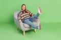 Full length body size photo laughing girl sitting in grey chair isolated pastel green color background