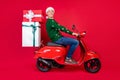Full length body size photo man smiling guy delivering gifts on motorbike isolated vivid red color background