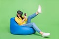 Full length body size photo of woman in beanbag playing video game in virtual reality glasses isolated bright green