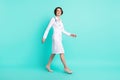 Full length body size side profile photo of nurse smiling going forward wearing white coat isolated bright teal color