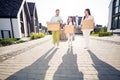 Full length body size view of three cheery family walking carrying packages cardboard belongings stuff to residence in Royalty Free Stock Photo