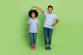 Full length body size view of two attractive trendy cheerful pre-teen kids measuring growth isolated over green color