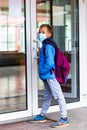 Full length boy wearing protective mask is trying to open the school door. Behind the backpack Schoolboy look at camera Royalty Free Stock Photo