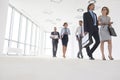 Full length of business colleagues walking while talking in office corridor Royalty Free Stock Photo