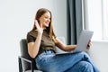 Young woman using laptop and speaking on smartphone while sitting in armchair against white studio wall, free space. Lovely young Royalty Free Stock Photo