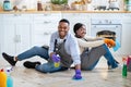 Full length of cheerful black couple resting on kitchen floor after cleaning flat, looking at camera and smiling