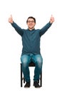 Full length cheerful and successful businessman, seated on a chair, shows thumbs up gesture, looking to camera isolated on white Royalty Free Stock Photo