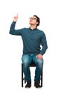 Full length contented businessman, seated on a chair, pointing forefinger looking up satisfied, isolated on white background. Royalty Free Stock Photo