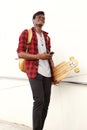 Full length cool african man with skateboard and mobile phone walking outdoors and smiling Royalty Free Stock Photo