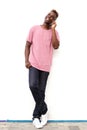 Full length cool young african man leaning against white wall and talking on mobile phone Royalty Free Stock Photo