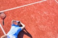 Full length of disappointed mature man with head in hands while lying by tennis racket on red court during summer Royalty Free Stock Photo