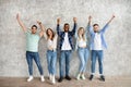 Full length of diverse friends holding hands up, feeling happy, looking at camera against grey studio wall Royalty Free Stock Photo