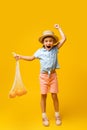 full length of excited kid in straw hat holding reusable string bag with oranges on yellow. Royalty Free Stock Photo