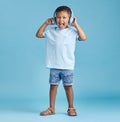Full length of an excited little boy listening to music with wireless headphones and wearing casual clothes against a Royalty Free Stock Photo