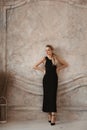 Full-length fashion portrait of a model girl with perfect slim body wearing a black evening dress posing in a minimalist Royalty Free Stock Photo