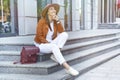 Full length of a fashionable happy woman wearing hat and backpack resting on city stairs, enjoying nice weather Royalty Free Stock Photo