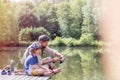 Full length of father assisting son fishing in lake while sitting on pier Royalty Free Stock Photo