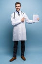 Full length of friendly doctor presenting empty digital tablet screen. Isolated on light blue. Royalty Free Stock Photo