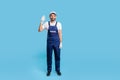Full length friendly handyman in overalls and protective gloves standing, waving hello, welcoming