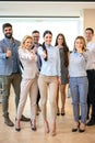 Full length of group of confident business people showing thumbs up standing close to each other and smiling at office. Royalty Free Stock Photo