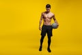 Full length of a handsome man with muscular body holding a basket ball, posing at studio, isolated yellow background. Royalty Free Stock Photo