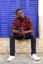 Full length handsome young african guy sitting outside with cell phone and earphones Royalty Free Stock Photo