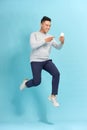 Full length of handsome  young man taking phone while jumping against blue background Royalty Free Stock Photo