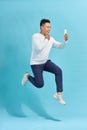 Full length of handsome young man taking phone while jumping against blue studio background Royalty Free Stock Photo