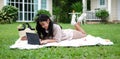 Full length of happy asian girl lying on the blanket in the garden and using laptop computer Royalty Free Stock Photo