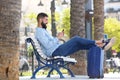 Full length happy man with cellphone and suitcase sitting on bench Royalty Free Stock Photo