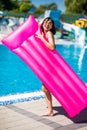 Full length of a happy pretty young girl wearing swimsuit standing near pool, holding inflatable pink mattress Royalty Free Stock Photo