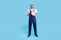 Full length happy punctual courier man in uniform holding clock and showing thumbs up, like gesture