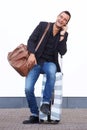 Full length happy travel man sitting on suitcase by white wall and talking with cellphone Royalty Free Stock Photo