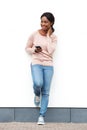Full length happy young african american woman standing against white wall with cellphone Royalty Free Stock Photo